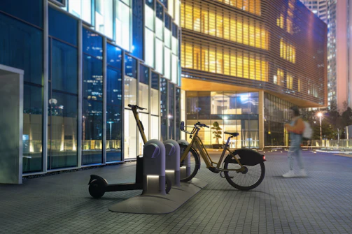 An electric bike charging at a modern urban charging station with a sunset backdrop.