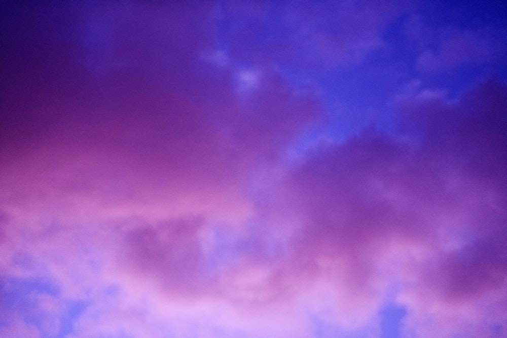 a plane flying in the sky with a purple and blue sky in the background