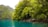 Lush green trees and vegetation line the edge of a turquoise body of water. Rocky cliffs covered with thick foliage are visible in the background, creating a natural, serene setting.