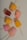 Several colorful popsicles arranged on a light speckled surface. Each popsicle is uniquely shaped and includes colors such as pink, yellow, and orange. Some of the popsicles have visible fruit chunks embedded inside.
