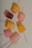 Several colorful popsicles arranged on a light speckled surface. Each popsicle is uniquely shaped and includes colors such as pink, yellow, and orange. Some of the popsicles have visible fruit chunks embedded inside.