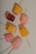 Several colorful popsicles arranged on a light speckled surface. Each popsicle is uniquely shaped and includes colors such as pink, yellow, and orange. Some of the popsicles have visible fruit chunks embedded inside.
