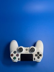 A white video game controller with various buttons, including directional and action buttons, placed against a solid blue background.