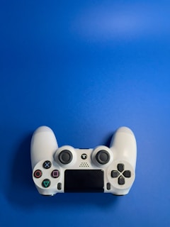 A white video game controller with various buttons, including directional and action buttons, placed against a solid blue background.