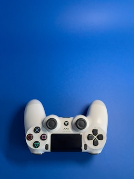 A white video game controller with various buttons, including directional and action buttons, placed against a solid blue background.