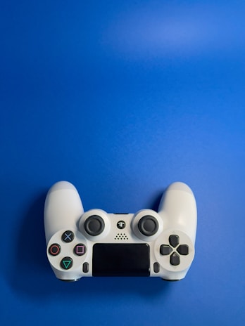 A white video game controller with various buttons, including directional and action buttons, placed against a solid blue background.