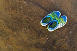 Close-up of colorful aqua shoes resting on sunlit sandy beach.
