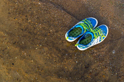 Close-up of colorful aqua shoes resting on sunlit sandy beach.