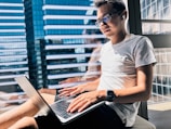 a man sitting in front of a window using a laptop computer