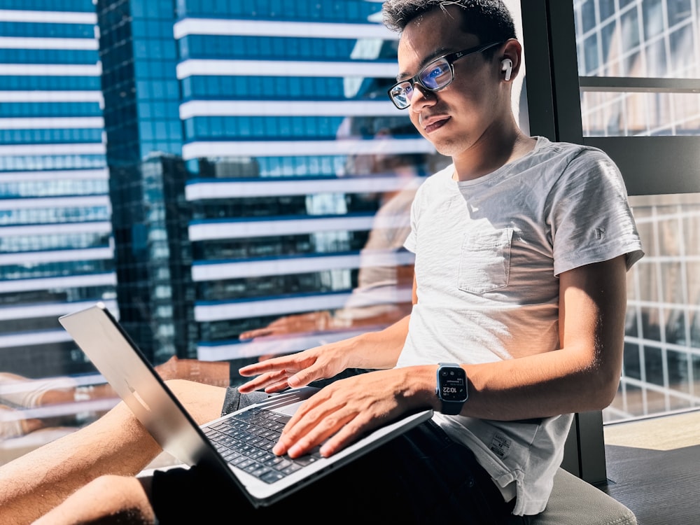 um homem sentado em frente a uma janela usando um computador portátil