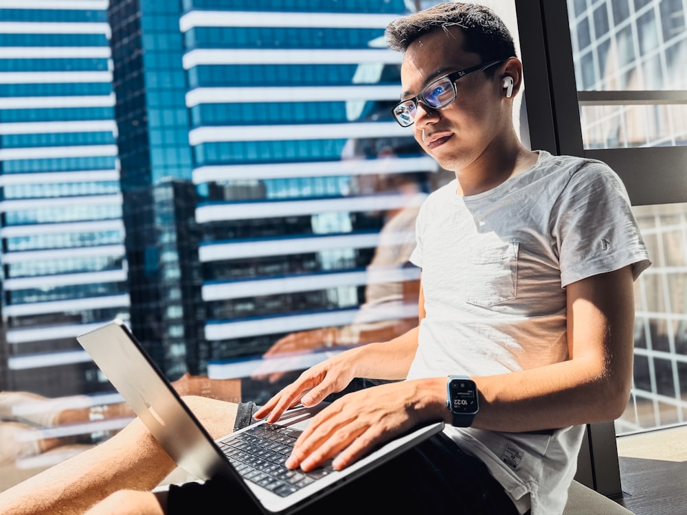 a man sitting in front of a window using a laptop computer