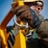 A close-up of a construction worker wearing a hard hat and gloves, gripping a yellow metal structure with a silver shackle. The image shows a focus on safety and attention to detail in a work environment.