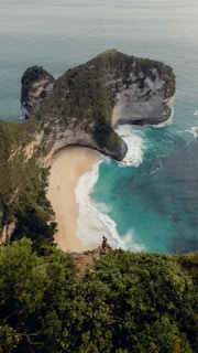 A panoramic coastal view from a cliffside lookout with a lone traveler capturing the moment