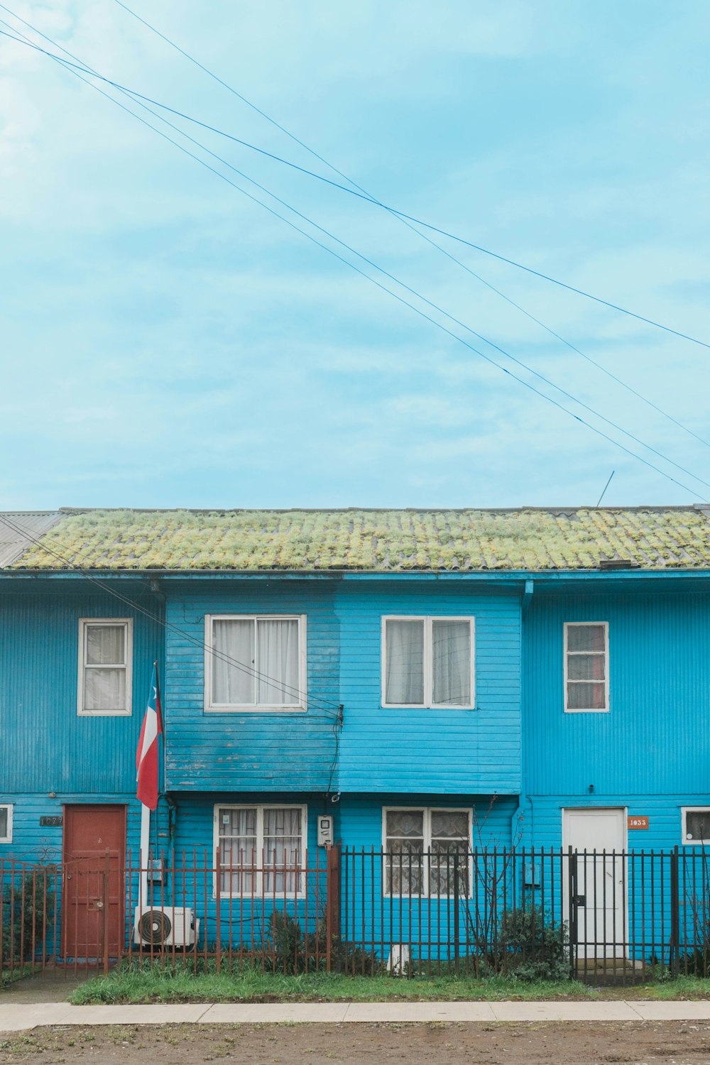 Un edificio blu con una porta rossa e una recinzione