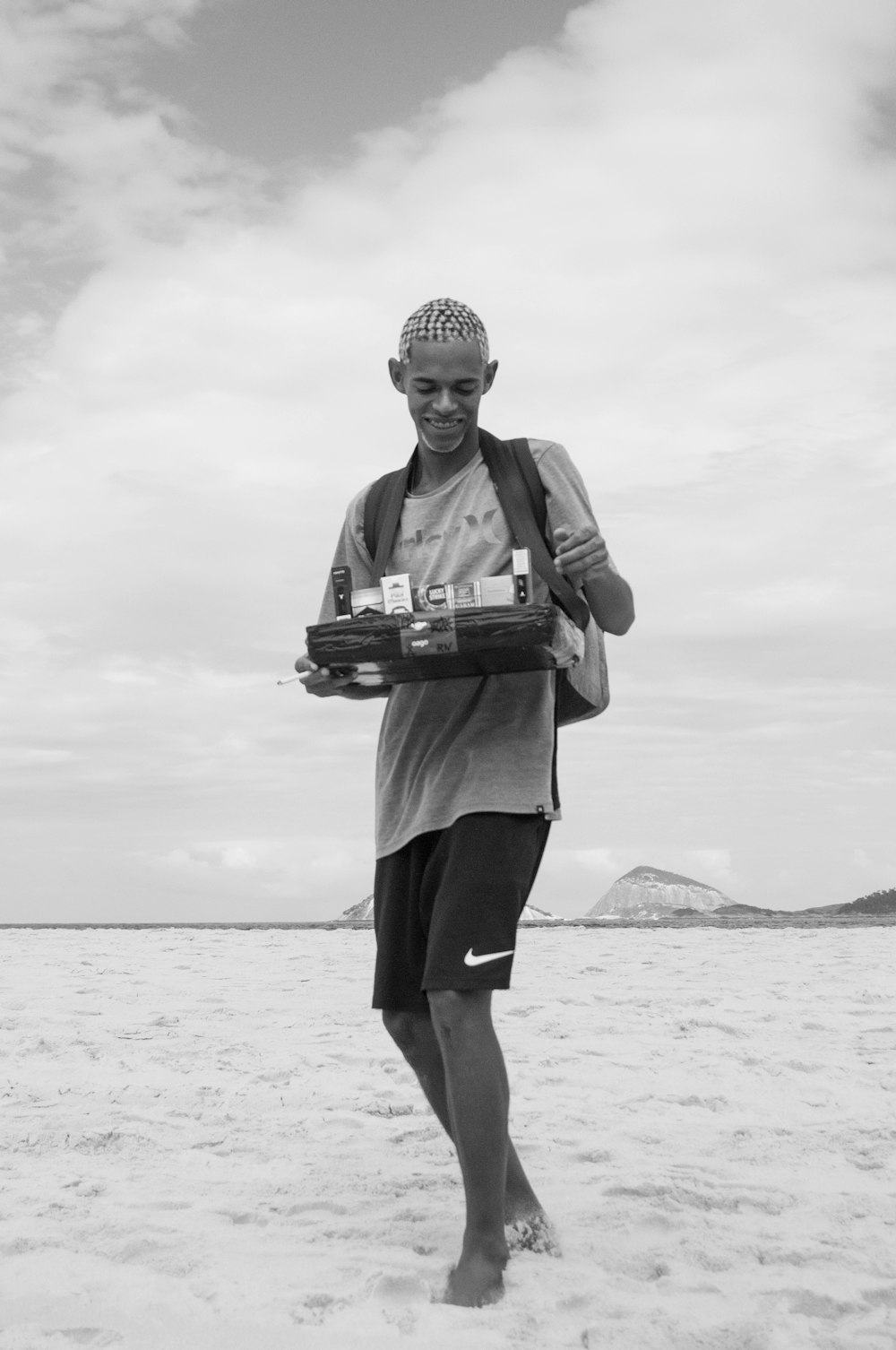 a man walking across a sandy beach holding a tray of food