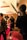 A film set scene with a group of people, including one person who appears to be acting, surrounded by cameras and lighting equipment. The setting has a warm, ambient lighting with decorations in the background and a red carpet on the floor.