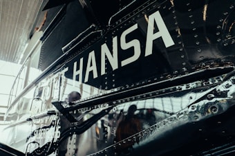 A close-up view of a metallic vehicle surface with rivets. The word 'HANSA' is prominently displayed in large white letters. The reflection on the surface suggests it could be an aircraft or a similar type of vehicle.