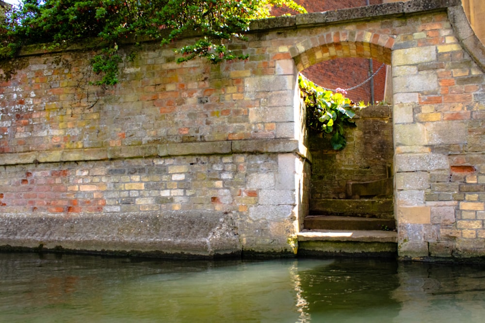 a brick wall with a doorway leading to a small body of water