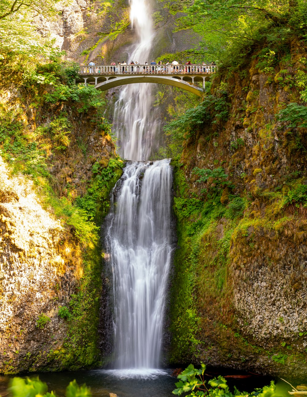 a waterfall with a bridge over it and people standing on it