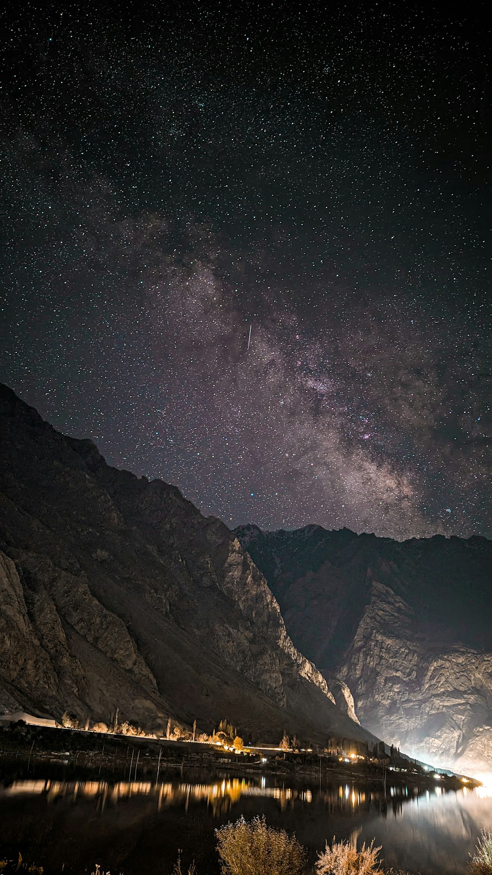 the night sky over a mountain range with a lake in the foreground