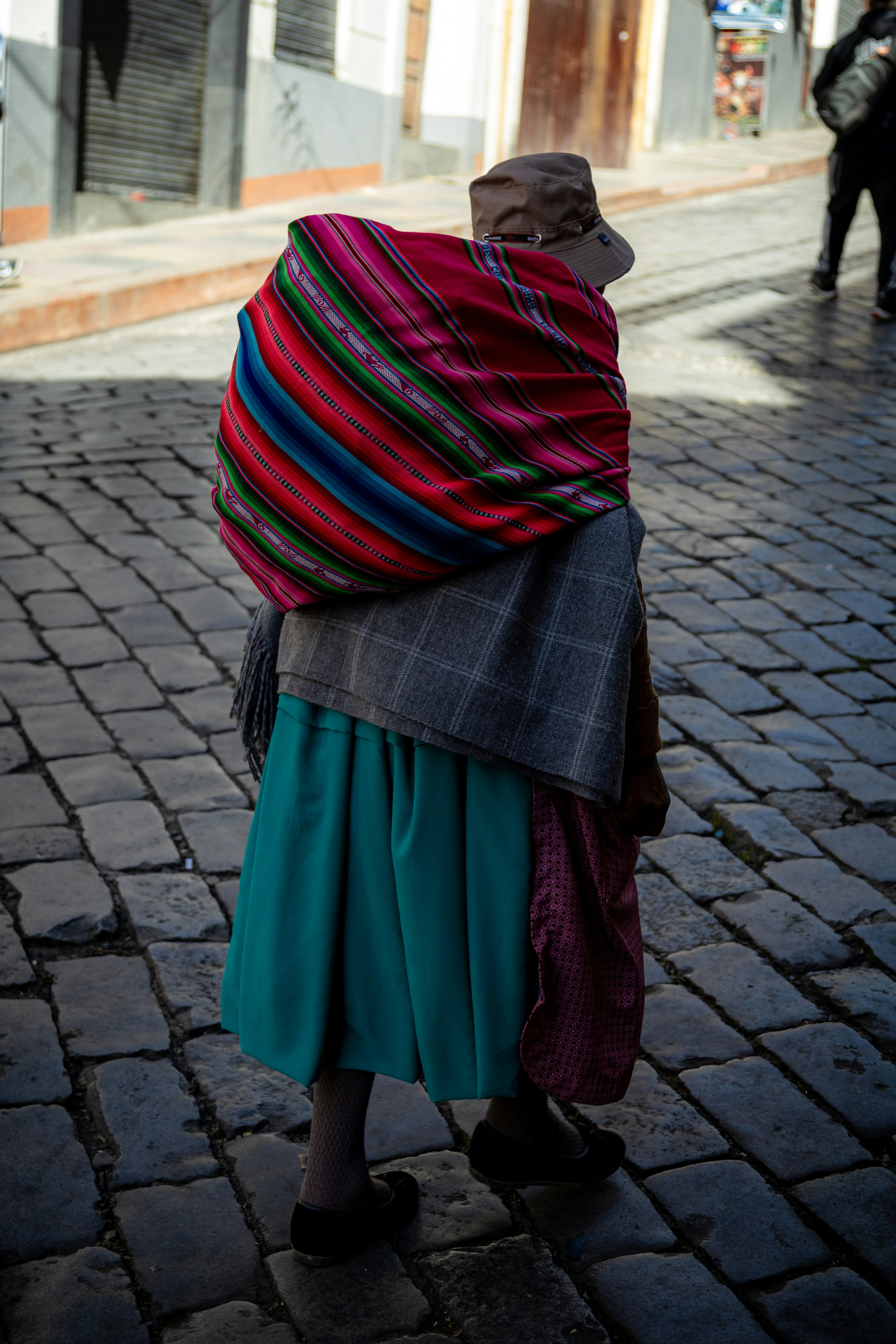 a woman walking down a street carrying a colorful blanket on her back