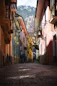 a narrow street with a few people walking down it