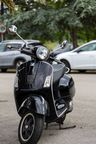 Close-up of a sleek black scooter parked on a city sidewalk near lush green trees of Central Park.