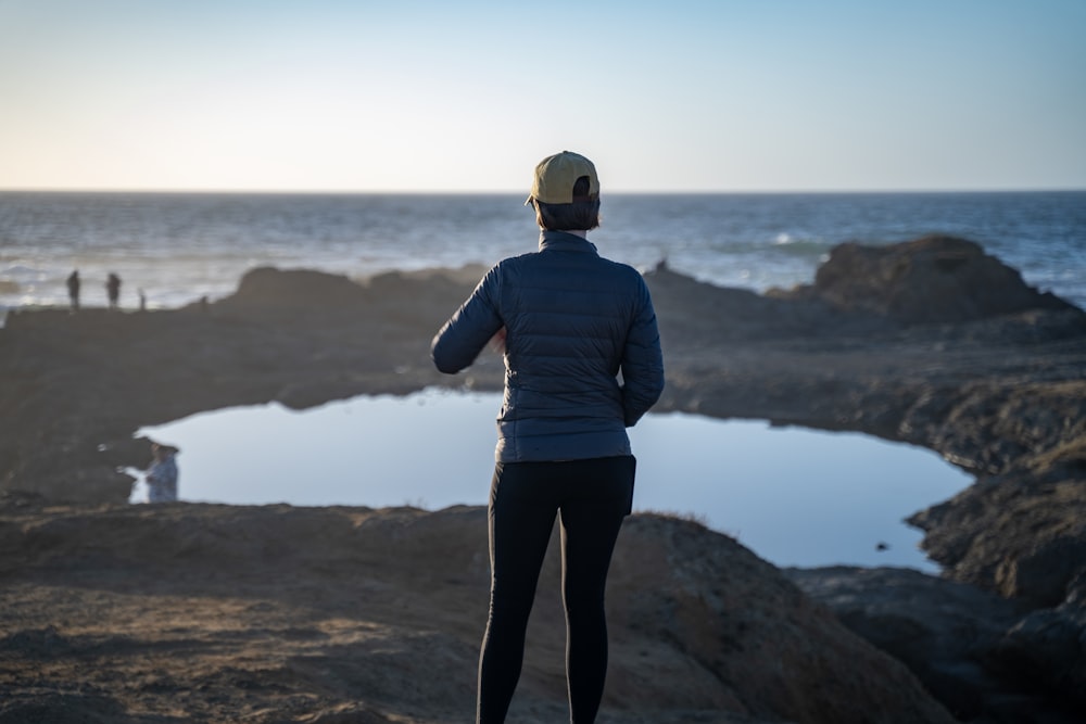 a woman standing on top of a rocky beach next to the ocean