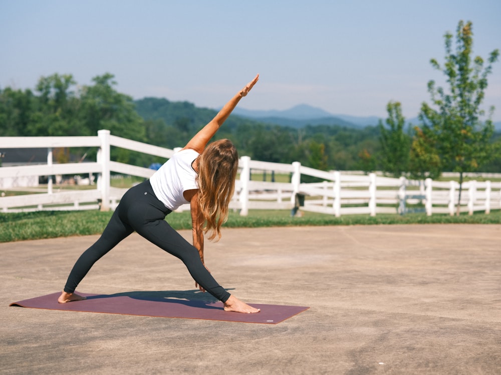 uma mulher de camisa branca e leggings pretas fazendo uma pose de ioga
