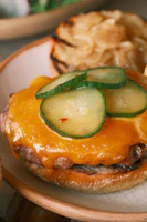 Close-up of a juicy smoked burger with melted cheddar and fresh pickles on a toasted bun.