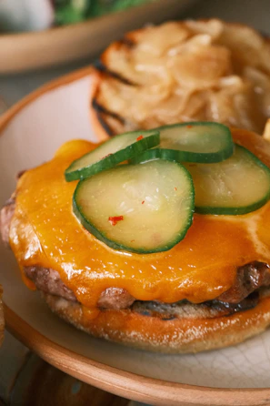 Close-up of a juicy smoked burger with melted cheddar and fresh pickles on a toasted bun.