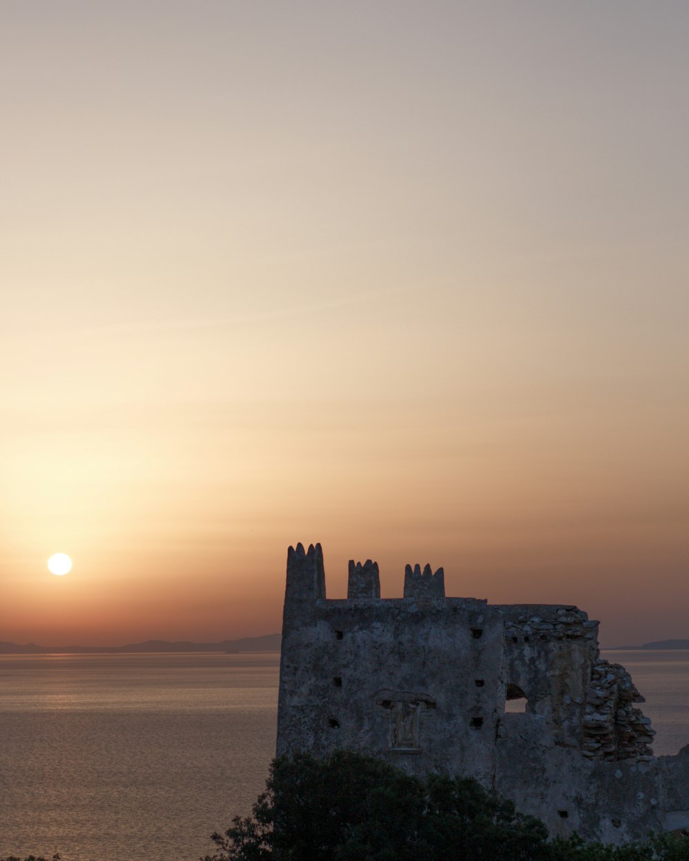 the sun is setting over a castle by the water