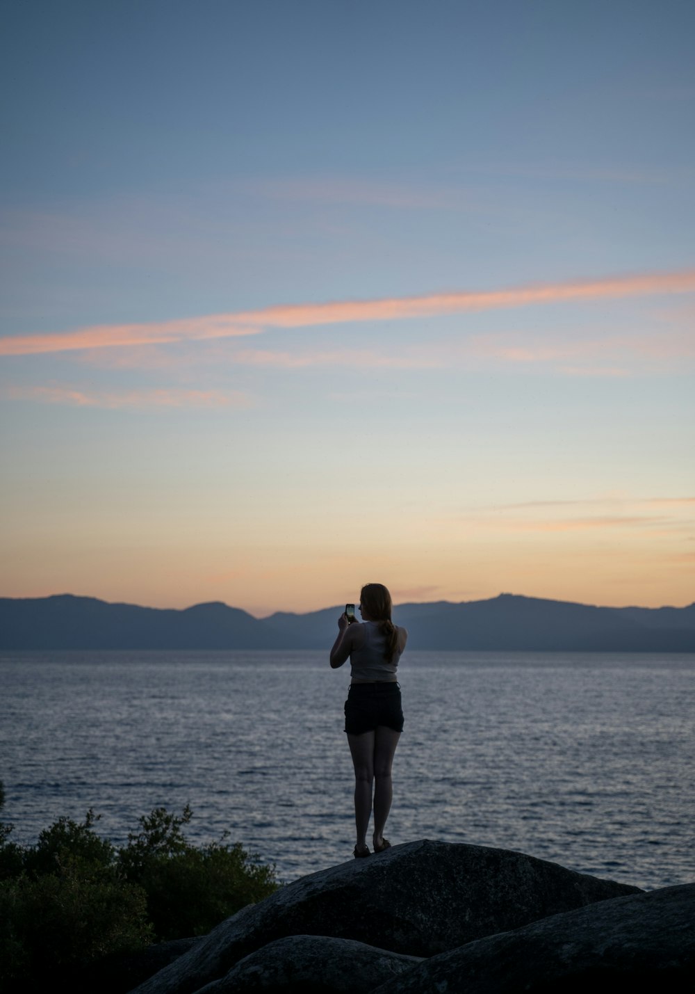 a woman standing on top of a rock next to the ocean
