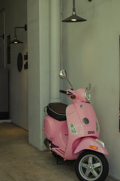 A glossy purple aan-g scooter parked against a matte silver wall with electric-blue lighting accents.