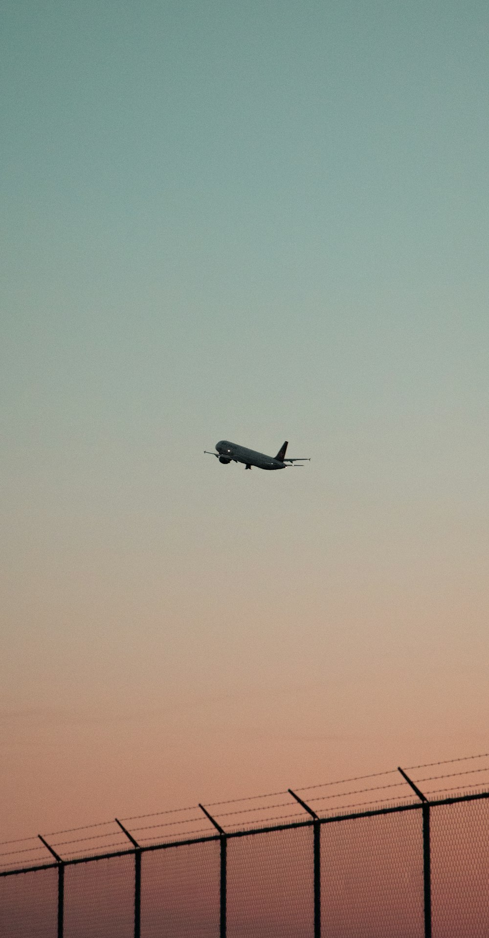 a plane is flying over a fence at sunset