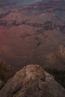 A vast, rugged canyon landscape with layers of rock formations and deep ravines, showcasing earthy textures and hues. The viewpoint overlooks an expansive vista, capturing the depth and grandeur of the natural environment.