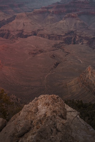 A vast, rugged canyon landscape with layers of rock formations and deep ravines, showcasing earthy textures and hues. The viewpoint overlooks an expansive vista, capturing the depth and grandeur of the natural environment.