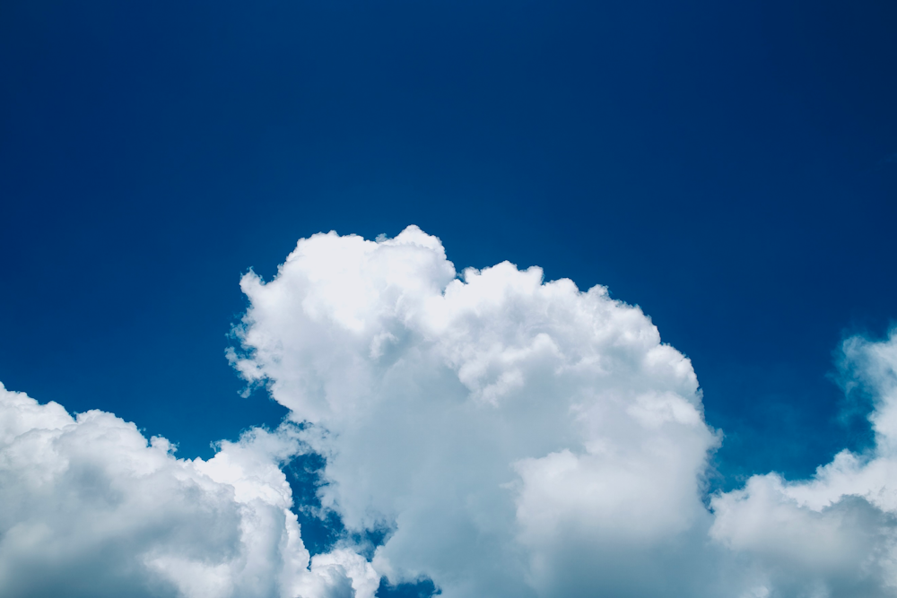 a plane flying through a cloud filled blue sky