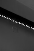 A row of small LED lights emitting a soft glow along the edge of a dark, flat surface. The surface appears smooth with a slight texture, possibly a wall or ceiling. The overall setting is dimly lit, creating a stark contrast between the lights and the surrounding darker area.