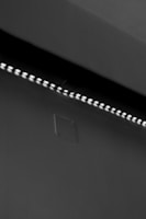 A row of small LED lights emitting a soft glow along the edge of a dark, flat surface. The surface appears smooth with a slight texture, possibly a wall or ceiling. The overall setting is dimly lit, creating a stark contrast between the lights and the surrounding darker area.