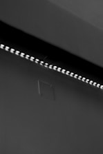 A row of small LED lights emitting a soft glow along the edge of a dark, flat surface. The surface appears smooth with a slight texture, possibly a wall or ceiling. The overall setting is dimly lit, creating a stark contrast between the lights and the surrounding darker area.