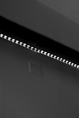 A row of small LED lights emitting a soft glow along the edge of a dark, flat surface. The surface appears smooth with a slight texture, possibly a wall or ceiling. The overall setting is dimly lit, creating a stark contrast between the lights and the surrounding darker area.