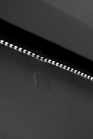 A row of small LED lights emitting a soft glow along the edge of a dark, flat surface. The surface appears smooth with a slight texture, possibly a wall or ceiling. The overall setting is dimly lit, creating a stark contrast between the lights and the surrounding darker area.