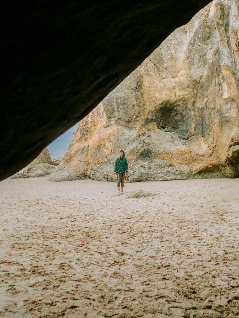 a man standing under a large rock on a beach