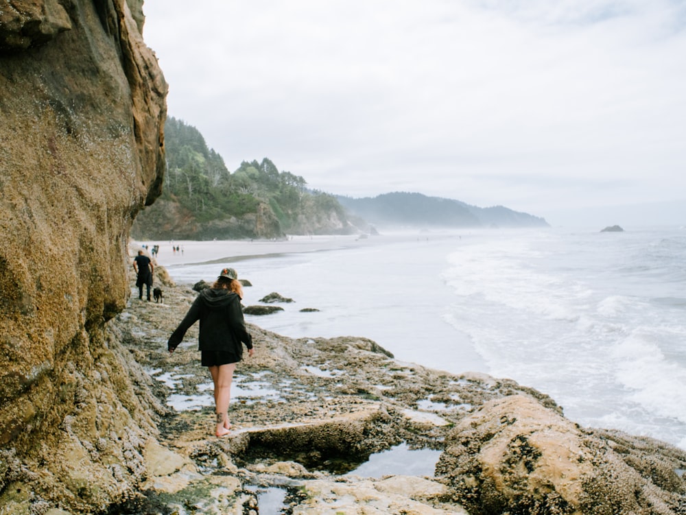 a woman walking along a rocky beach next to the ocean