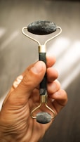 A hand is holding a jade roller, an object typically used for facial massage. The roller is made of a handle and two stone rollers, one larger at the top and one smaller at the bottom, both made from dark green jade.
