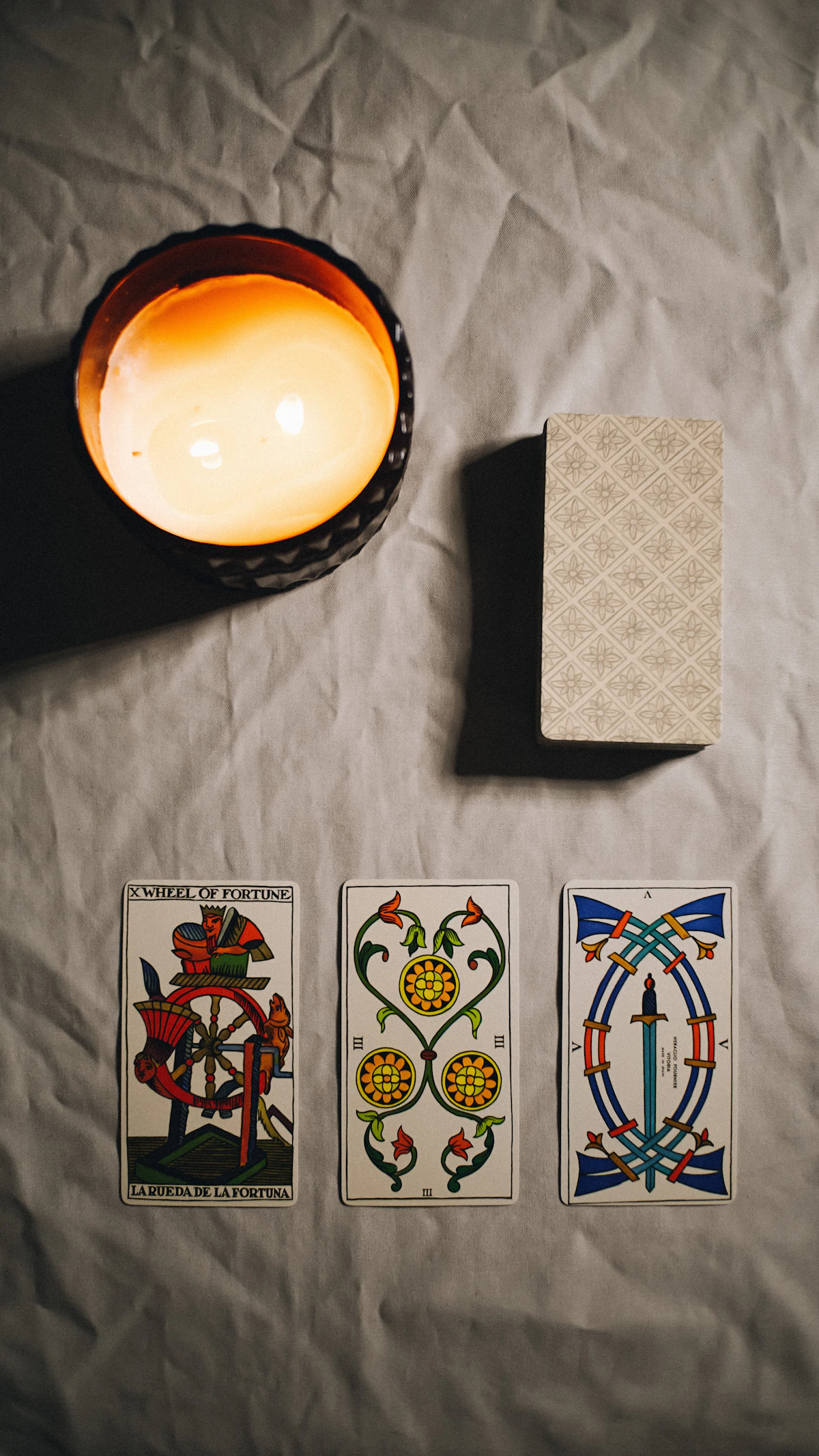 A lit candle beside a tarot deck with three cards laid out
