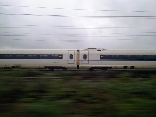 A sleek bullet train speeding past lush green fields under a clear blue sky.