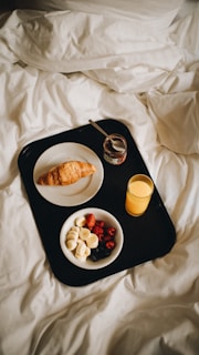 a tray of food on a bed with a glass of orange juice