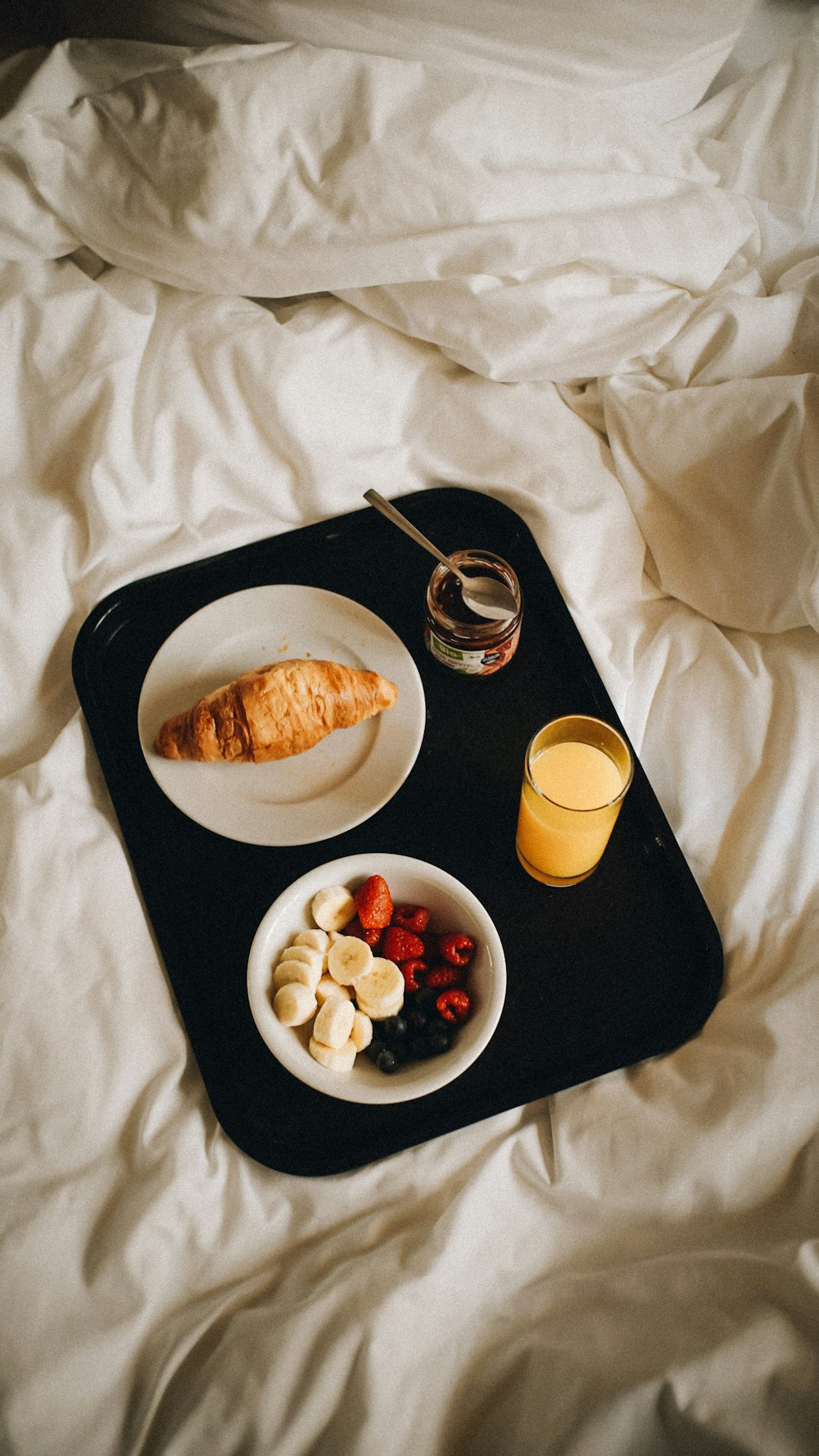 a tray of food on a bed with a glass of orange juice